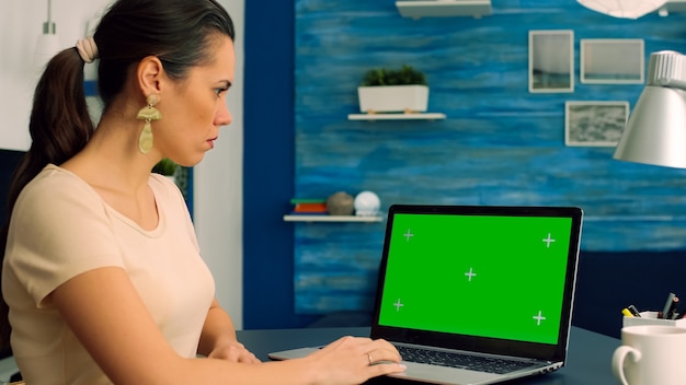 Business woman working at marketing project from home office using laptop computer with green screen chroma key display