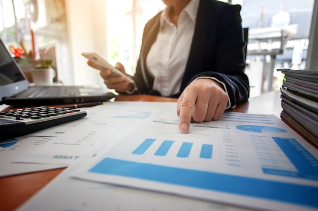 Business woman at working with financial reports and using mobile smartphone in the office