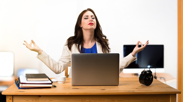 Business woman working with her laptop and in zen position in the office