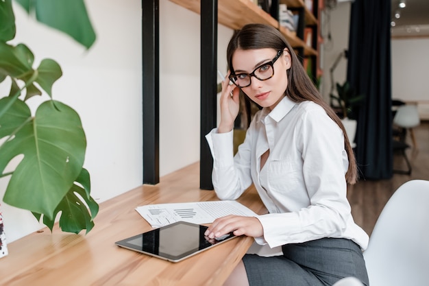 ビジネスの女性は、タブレットとグラフを使ってオフィスで働いています