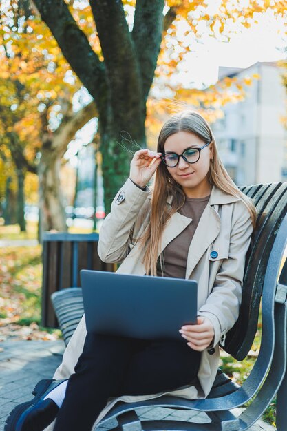 Una donna d'affari lavora con un computer portatile in autumn park ha un grande sorriso capelli lunghi e grandi occhi azzurri ritratto di una moderna donna che lavora sfondo giallo del parco