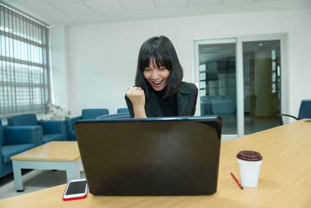 ラップトップからすごいビジネスウーマン株式市場を見て幸せなタイの女性のコンセプトオフィスで働く秘書