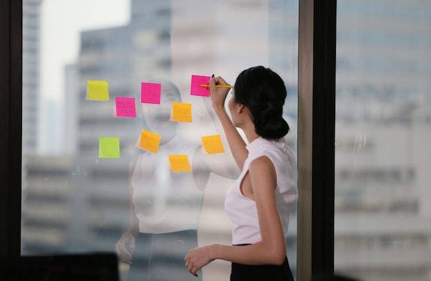 Photo business woman writes notes on the paper attached to the window glass