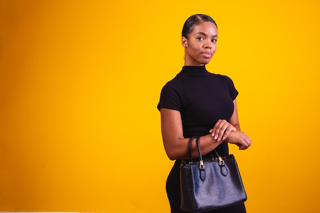 Business woman on yellow background wearing black clothes and hand bag.