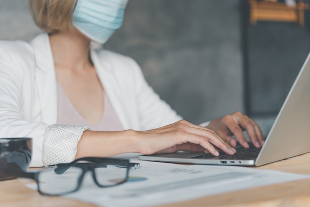 Business womanl wears a mask to protect against viruses, sit on a laptop, newnormal during the coronavirus epidemic