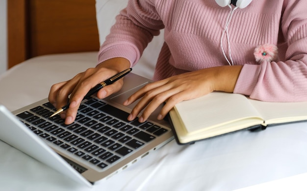 La mano del contabile delle donne d'affari che tiene la penna e usa il computer portatile facendo il conto per pagare le tasse sul letto, lavora dal concetto di casa.