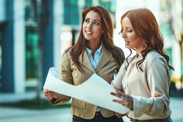 Business women is standing and holding paper documents outside against urban city background.