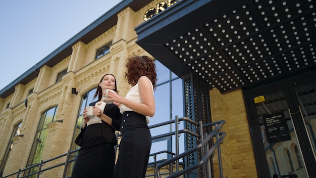 Business women talking near office Smiling ladies standing with cups outdoors