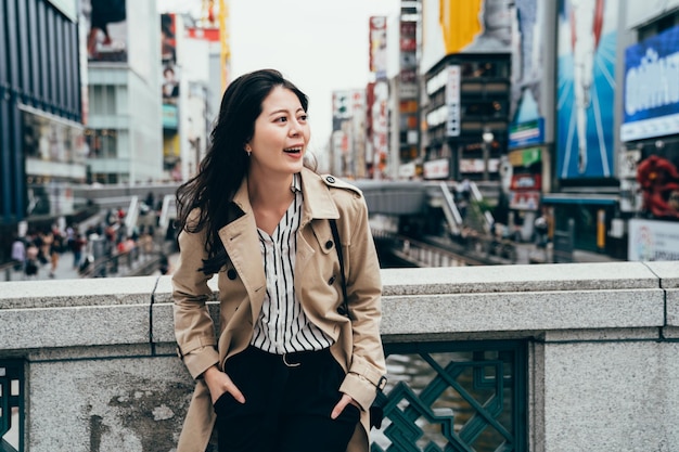 business worker looking the beautiful canal view standing on the bridge above the river laughing cheerfully. office lady relying on the handrail in dotonbori osaka japan. woamn in smart casual suit.