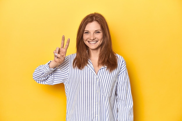 Businessdressed redhead formal studio shot joyful and carefree showing a peace symbol with fingers