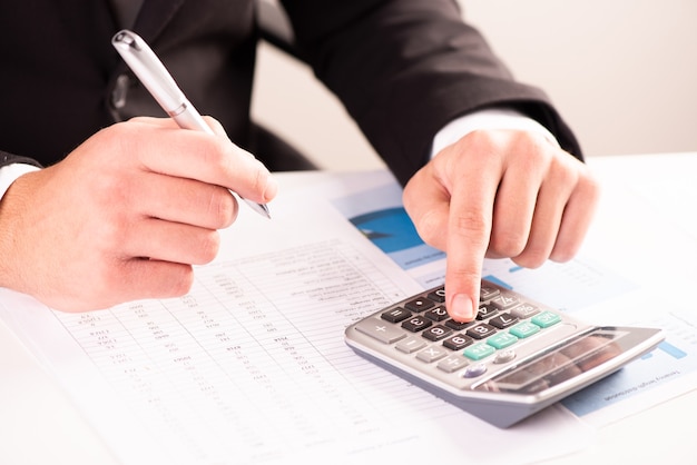 Бизнесмен, анализирующий счет, инвестиции и графики с калькулятором на столе