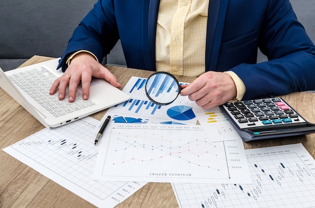 Businessman analyzing business graphs with magnifying glass