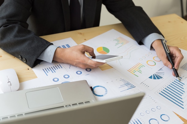 Businessman analyzing charts and graphs with smartphone.