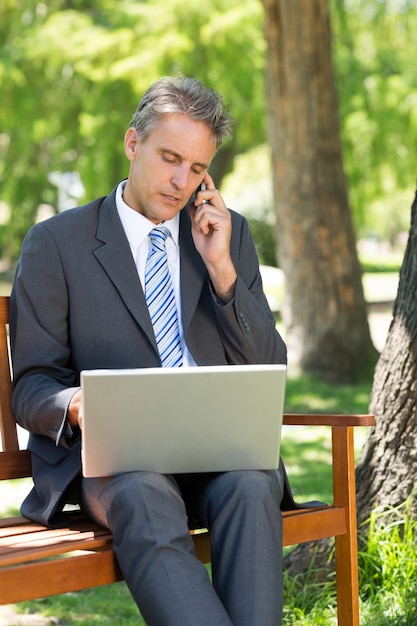 Businessman answering cellphone while using laptop