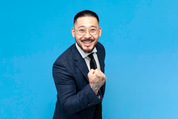 businessman asian winner in suit and glasses rejoice and celebrate victory on blue background