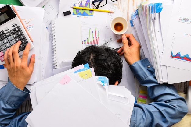 Businessman asleep at office desk with finance sheet calculator and coffee.