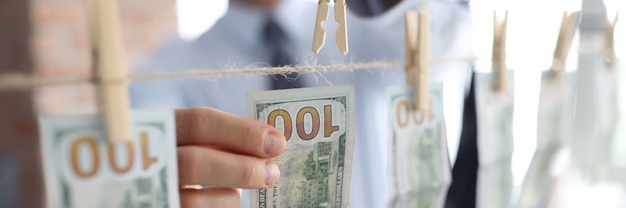 Businessman attaches one hundred dollar bills on clothespins to rope.