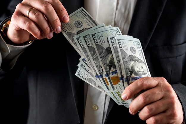 Businessman or bank employee counting one hundred dollar bills in front of him with his hands