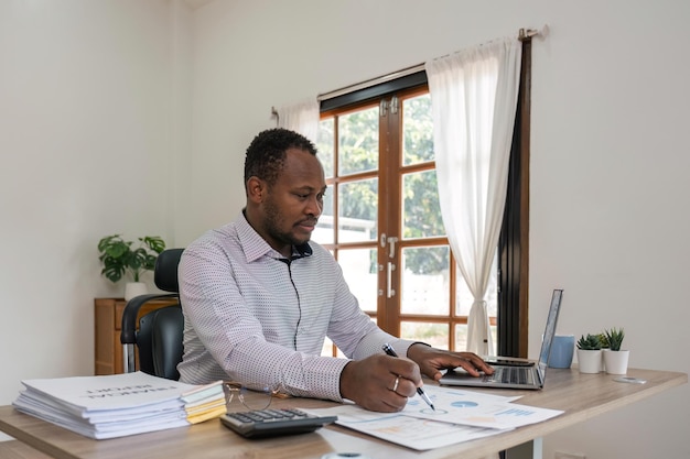 Businessman black man using laptop at home in living room Happy mature businessman send email and working at home African american man typing on computer with paperworks and documents on table