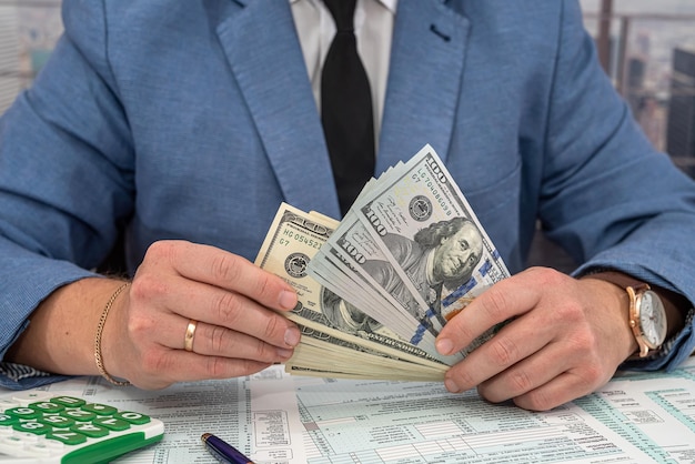 Businessman in a black stylish suit at a spacious table counts\
dollars and fills out forms