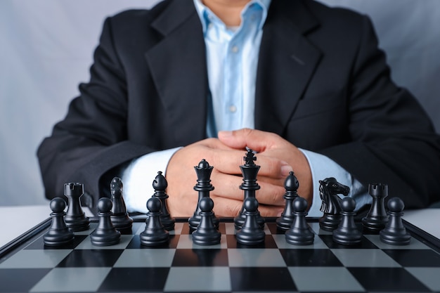 Бизнесмен в черном костюме сидит и контролирует команду впереди к положению успеха на соревновательной деловой игре в шахматы.