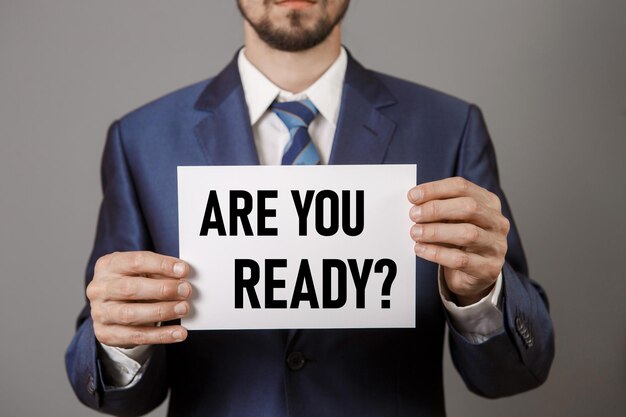 Businessman in blue fashionable business suit holding a white paper with inscription ARE YOU READY