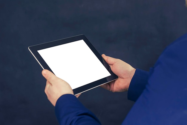 Businessman in a blue jacket holds a mockup of a tablet with a white screen on a dark background