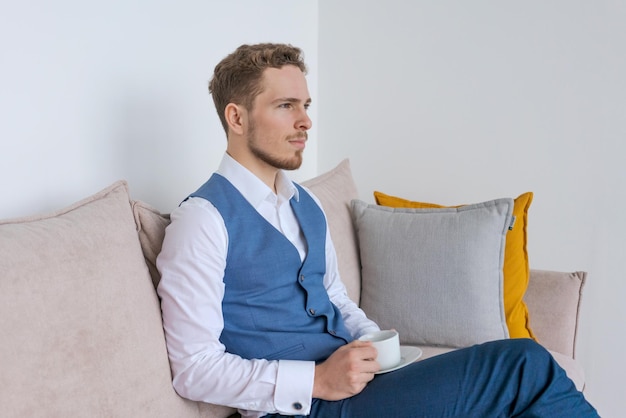 Businessman in blue suit sitting in his office sofa sits with\
coffee cup