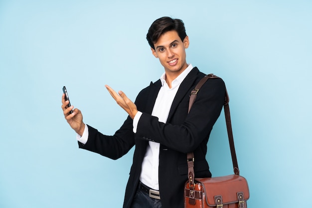 Businessman over blue wall extending hands to the side for inviting to come