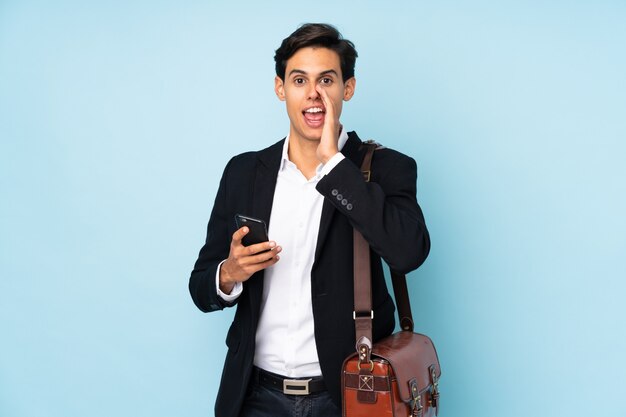 Businessman over blue wall shouting with mouth wide open