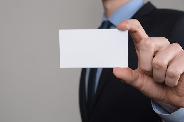 Бизнесмен, деловой человек держит руку, показывая визитную карточку крупным планом выстрелил на серый