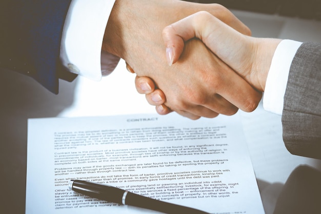 Businessman and business woman shaking hands to each other above signed contract. Success at negotiation and agreement concept