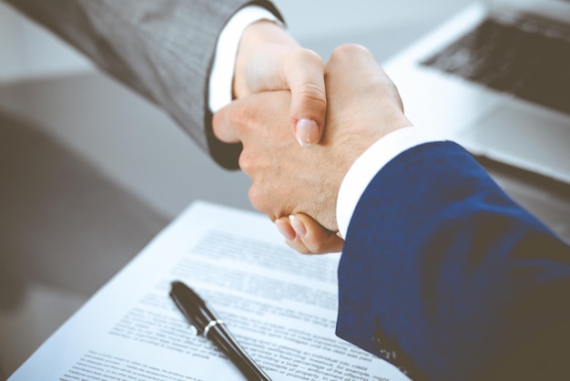 Бизнесмен и бизнесменка пожимают друг другу руки над подписанным контрактом. Успех в переговорах и концепции соглашения
