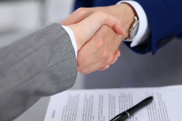 Businessman and business woman shaking hands to each other above signed contract.