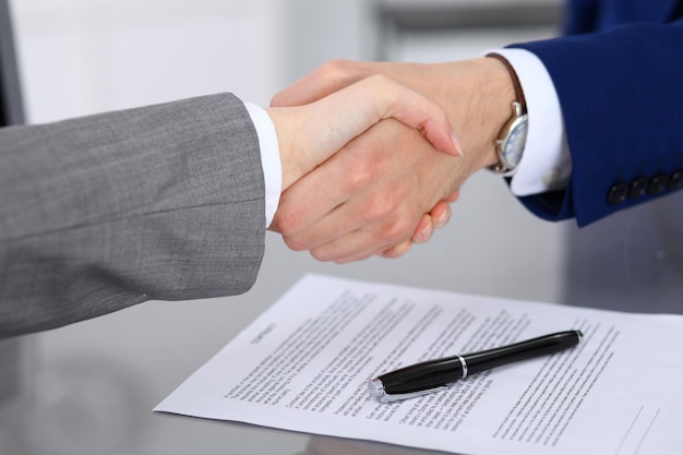 Businessman and business woman shaking hands to each other above signed contract.