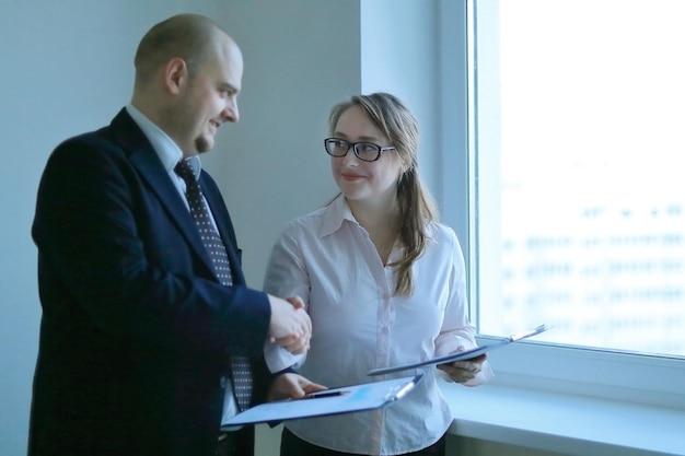 Businessman and business woman shaking hands standing near the window