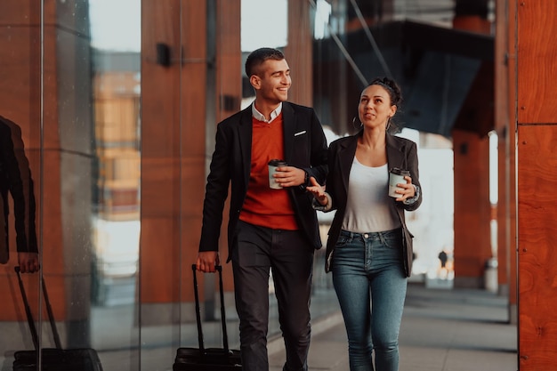 Photo businessman and businesswoman talking and holding luggage traveling on a business trip, carrying fresh coffee in their hands. business concept. high-quality photo