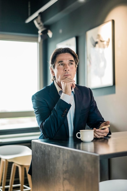 Businessman in cafeteria with cup of coffee thinking