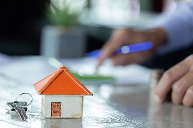 Businessman calculating house costs using calculator with house model and key on desk