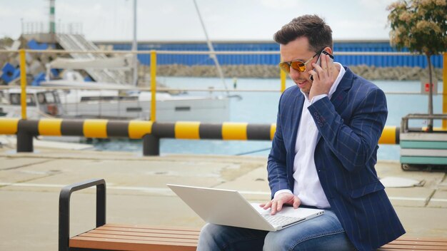 Photo businessman calling by mobile phone and working on laptop outdoors