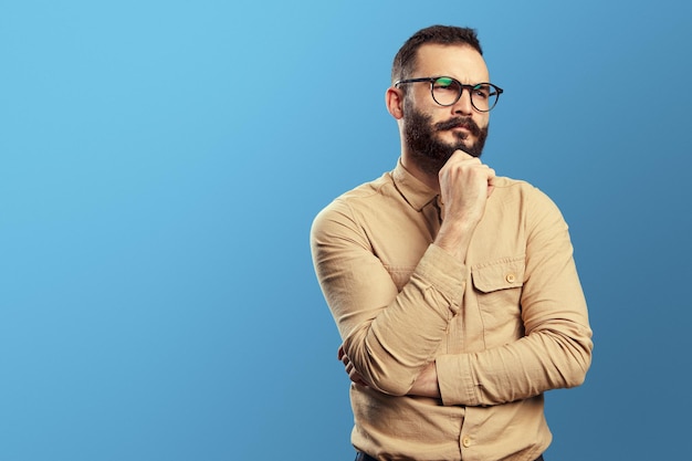 Businessman in casual beige shirt touching chin and looking with suspicion