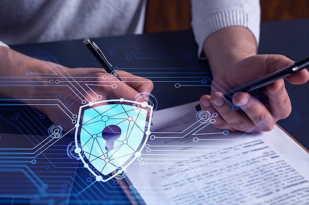 A businessman in casual wear signing the contract to prevent probability of risks in cyber security Checking the phone Padlock Hologram icons over the working desk