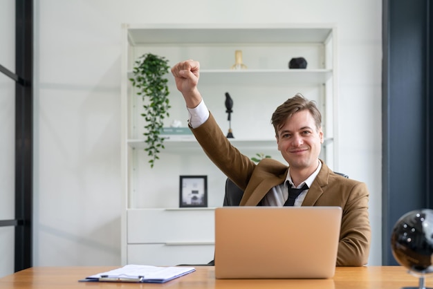 Uomo d'affari che celebra il successo con il braccio che alza il pugno mentre è seduto alla scrivania in ufficio