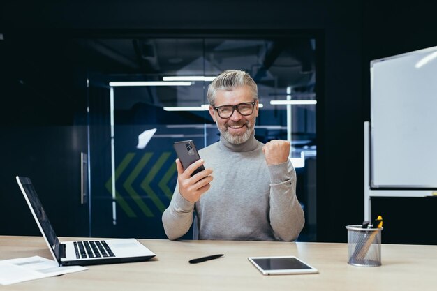 Businessman celebrating victory and success mature gray haired man inside office got good news