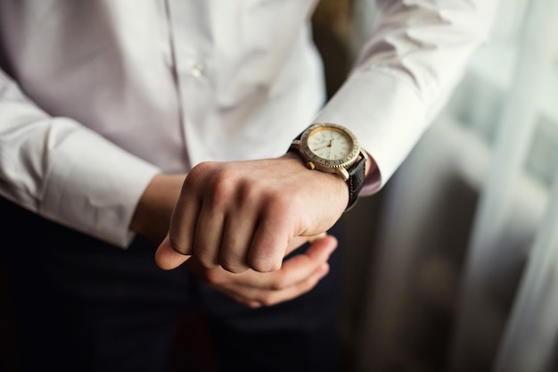 Uomo d'affari che controlla tempo sul suo orologio da polso, uomo che mette l'orologio a disposizione, sposo che si prepara al mattino prima della cerimonia di nozze