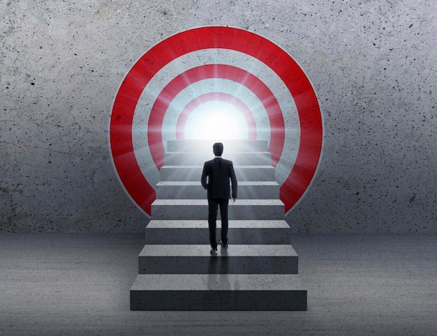 Businessman climbing concrete stairs toward a red dartboard with shining target background