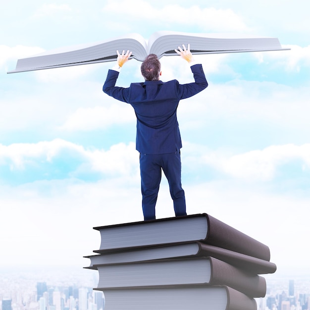 Businessman climbing on a cube with arms out against city on the horizon