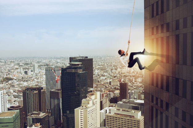 Businessman climbs an high building with a rope