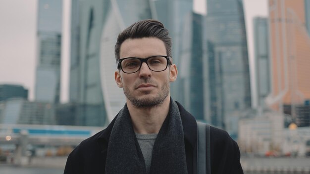 Businessman in coat and eyeglasses on background of skyscrapers business centre