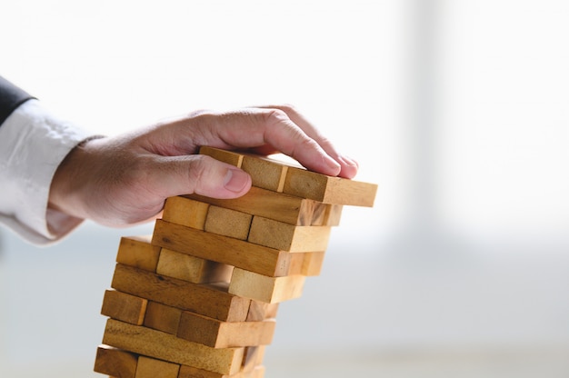 Businessman collapsing stacked tower wood block by hand as failure or bankrupt project. 